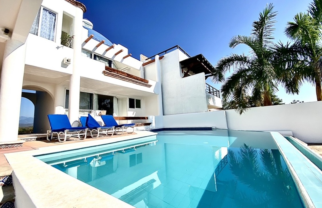 Modern white villa with a private pool, palm trees, and blue lounge chairs.