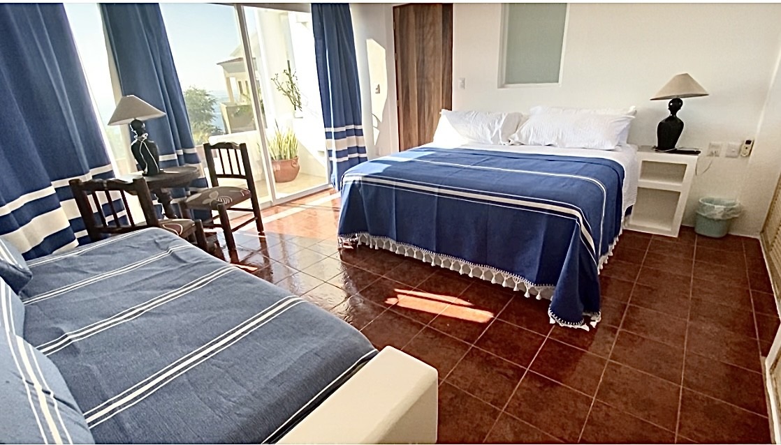 A bright hotel room with a king bed and a small sofa, both with blue and white linens