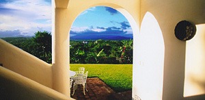 Sunlit archway overlooking a green garden and distant mountains.