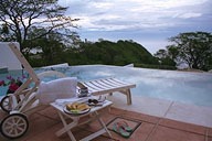 Poolside scene at sunset with a lounge chair, drink trolley, and snacks.